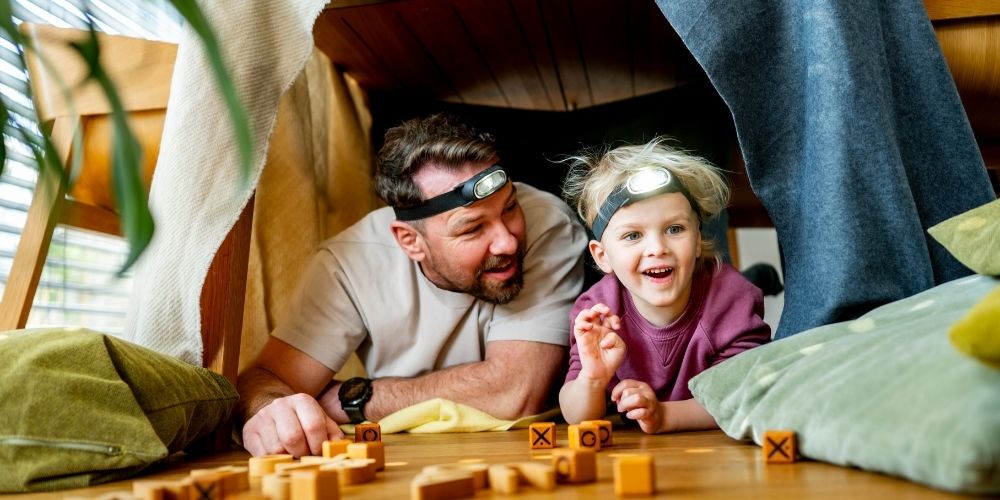 Dad with his kid inside a fort they built in the living room.